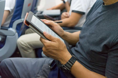 Casually dressed middle aged writer man working on Electronic book (Ebook) in aircraft cabin during...