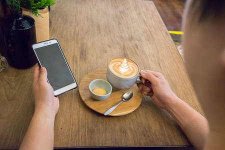 Businessman holding a cell phone while drinking coffee on wood tableの写真素材
