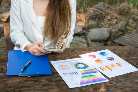 Business analysis - calculator, sheet, graphs (business report) and analyst hand with her phone on...