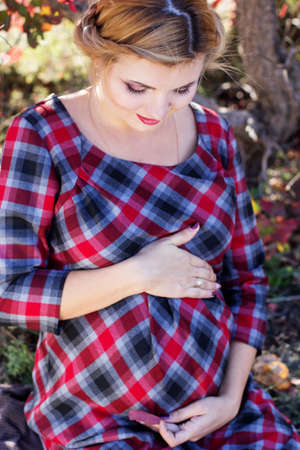 Pregnant girl is wearing checkered dress in park