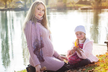 Little girl with her mother on the autumn lakeの写真素材