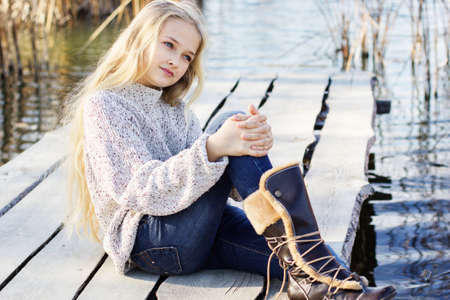 Little cute girl outdoors is sitting near lake and wearing fashion dress. Portrait caucasian female...