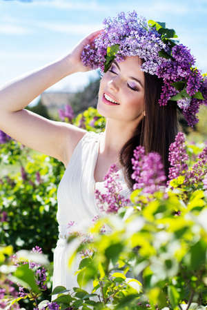 Beautiful smiling girl is wearing beautiful wreath of lilac flowers in spring gardenの写真素材