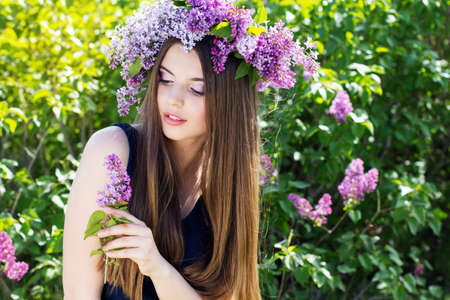 Beautiful smiling girl with fashion makeup is wearing beautiful wreath of lilac flowers, spring timeの写真素材