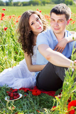Young happy couple man and woman reasting on a meadow full of poppiesの写真素材