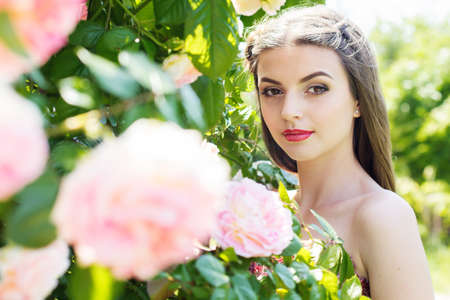 Portrait of beautiful young girl with fashion makeup posing near pink roses in a gardenの写真素材