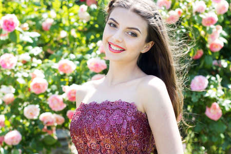 Portrait of beautiful smiling young girl with fashion makeup posing near pink roses in a gardenの写真素材