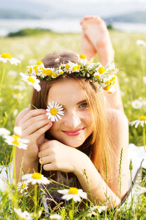 Cute smiling child girl is lying at green field with camomiles flowersの写真素材