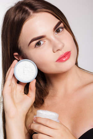 Portrait of attractive caucasian girl with perfect skin isolated on white in studio is holding jar of face wrinkle creamの写真素材