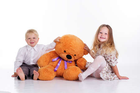 Beautiful child girl and boy are embracing big brown teddy bear, isolated on whiteの写真素材