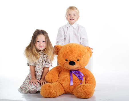 Beautiful happy children are embracing big brown teddy bear, isolated on whiteの写真素材