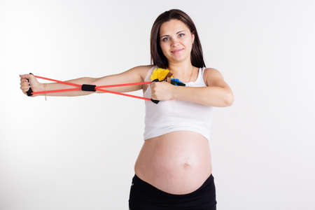 Pregnant woman doing stratching exercises with resistance bands tube isolated on white in studioの写真素材