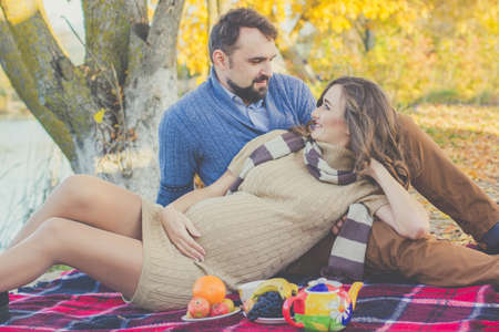 Happy future parents are spending time on the picnic in autumn parkの写真素材