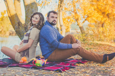 Happy future parents woman and man are wearing warm clothes spending time on the picnic with tea and...