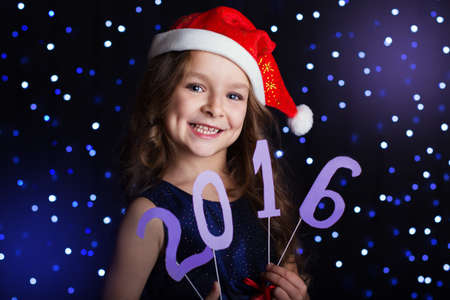Happy child girl is holding numbers 2016 in hands in a studio background scene with lights for a...