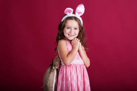 Cute little girl is wearing pink bunny ears on red backgroundの写真素材