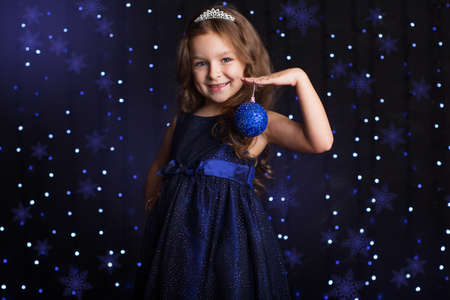 Happy child girl is with blue Christmas tree toy in hands over background scene with lights, New yearsの写真素材