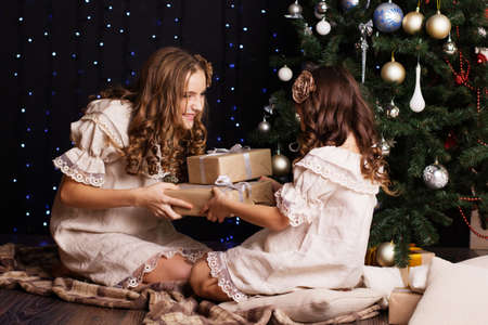 Pretty two sisters are sharing gift boxes at home near christmas treeの写真素材