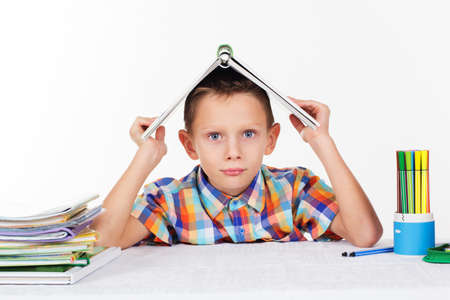 Cute little serious sad boy is holding book on his head, isolated over white backgroundの写真素材