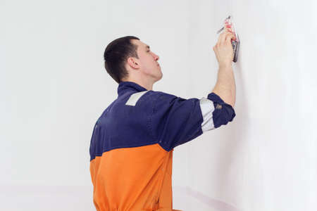 Handyman is doing grinding works with sandpaper on a white wall in roomの写真素材