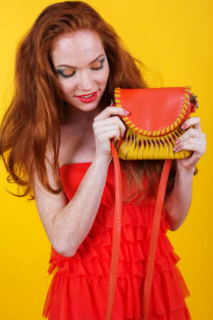 Portrait of beautiful redheaded girl with fashion colorful makeup is holding orange purseの写真素材