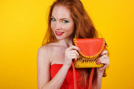 Portrait of beautiful redheaded girl with fashion colorful makeup is holding orange fashion purseの写真素材