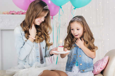 Two pretty girls are celebrating birthday in a studio with blue and pink balloonsの写真素材