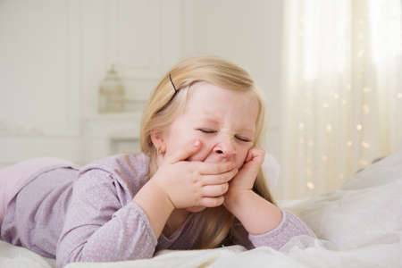 Happy blonde girl is yawning in the bedの写真素材