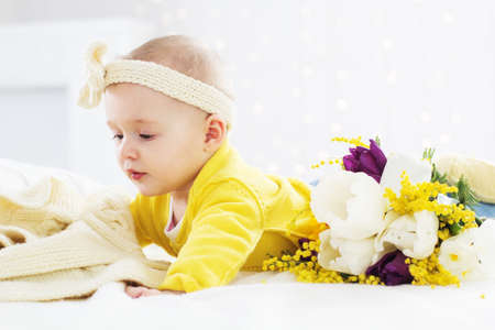Little baby girl is lying on bed with flowersの写真素材