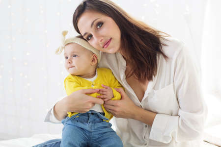 Happy young mother with baby girl are sitting on bed