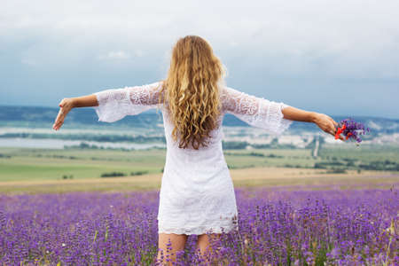 Beautiful smiling woman is wearing nice wedding dress dancing at field of purple lavender flowersの写真素材