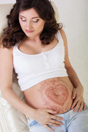 Pretty pregnant woman with fashion makeup and henna tattoo mehendi on her belly in studio