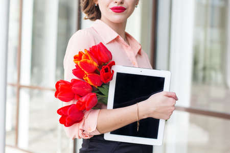 Beautiful business woman in springtime. Woman with bouquet of red tulips and digital tabletの写真素材