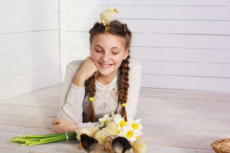 Happy smiling teenager girl is lying on wooden floor with yellow small chick in her headの写真素材