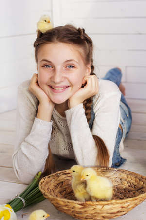Happy smiling teenager girl is lying on wooden floor with yellow small chick in her head and in basketの写真素材