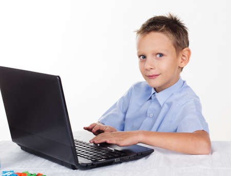 Pretty boy is doing homework with laptop, isolated over white background