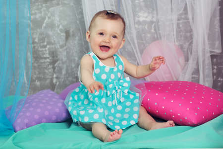 Happy cute baby girl is wearing nice dress sitting with colorful pillows