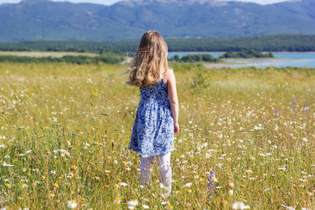 Cute pretty child girl is staying in green field over mountains viewの写真素材