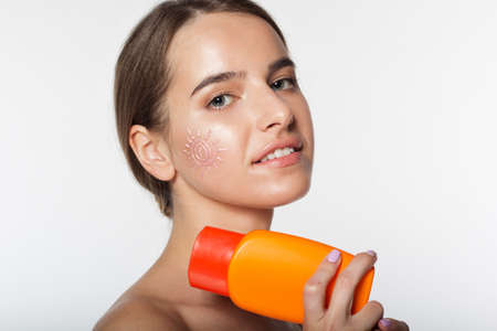 Studio portrait of beautiful natural girl is holding sunscreen tanning lotion in hands