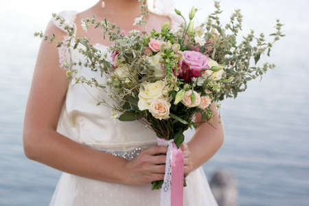 Fashion bouquet with roses in hands of young beautiful bride over blue sea backgroundの写真素材