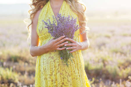 Closeup picture of belly of pregnant woman is holding bouquet of lavender flowersの写真素材