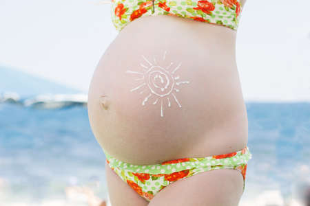 Pregnant woman with sunscreen cream uv protection on her belly in sun shapeの写真素材