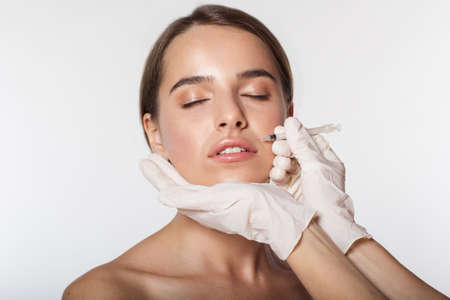 Young woman getting beauty injection by doctor in white gloves isolated on whiteの写真素材