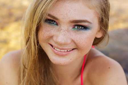 Portrait of smiling teenager girl with freckles over her face and fashion makeup is wearing bikini resting on the beachの写真素材