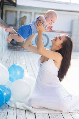 Beautiful smiling mother is wearing white dress with little baby boy are enjoying nice sunny day...