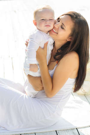 Beautiful smiling mom is wearing white dress with little baby boy are enjoying nice sunny dayの写真素材