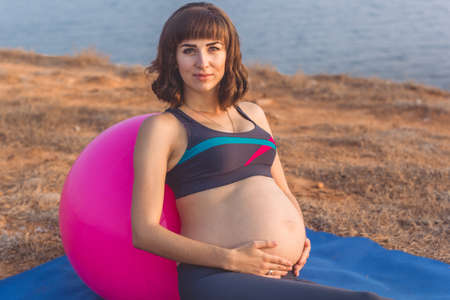 Pregnant woman with pink fitball on the beach