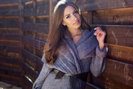 Young beautiful woman is wearing warm clothes near wooden wallの写真素材
