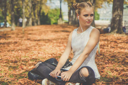 Pretty schoolgirl girl is relaxing on autumn leaves with digital tablet and listening music