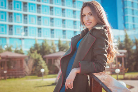 Young fashion smiling girl with long hair in wooden bridge is wearing warm dark coat infront of blue buidingの写真素材